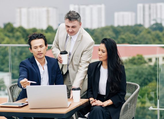 Serious business executives sitting at table at rooftop cafe and discussing data on laptop screen